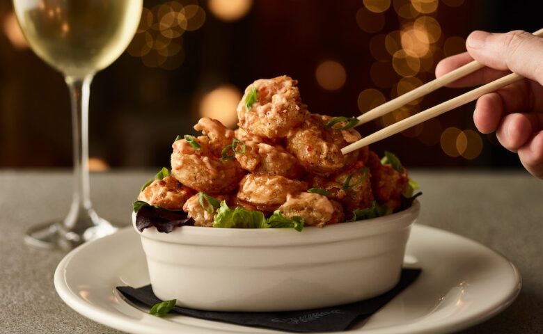 a bowl of fried shrimp with chopsticks reaching into the frame