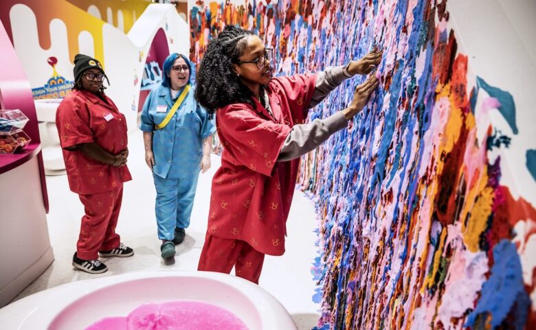 person touching a colorful slime wall white two more people look surprised int he background
