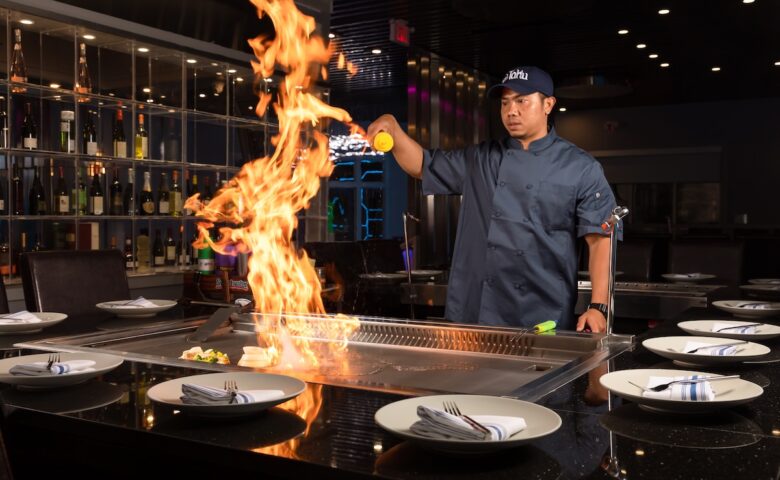 person pouring something onto a fire on. a large grill