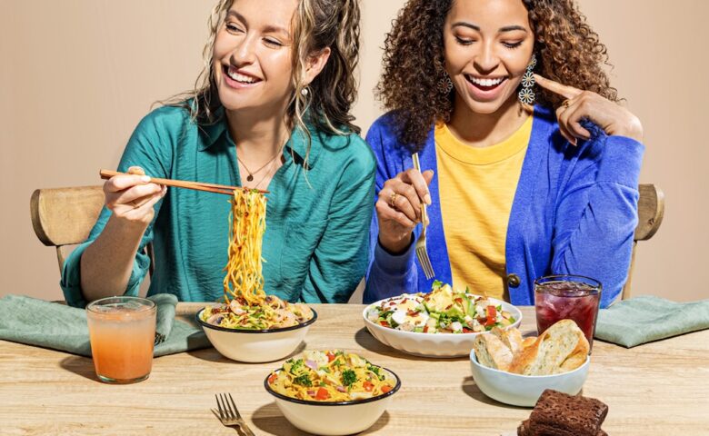 twoe people in brightly colored clothing eating stir fry and salad